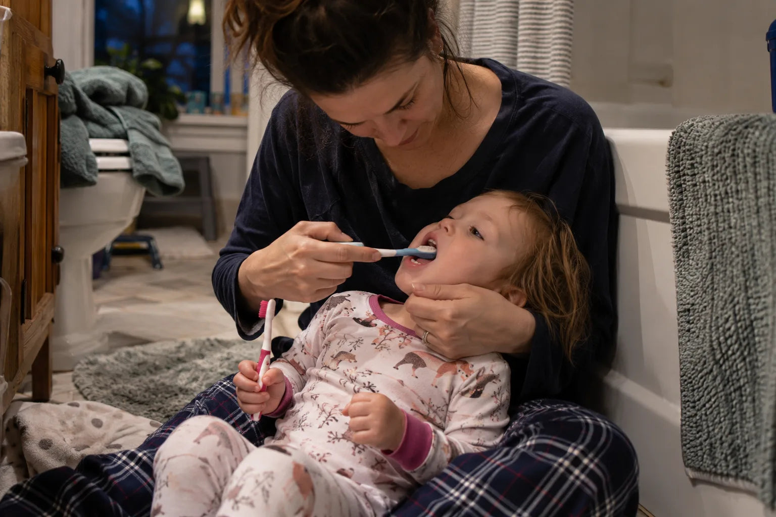 A parent brushing a toddler's teeth with the toddler lying in their lap