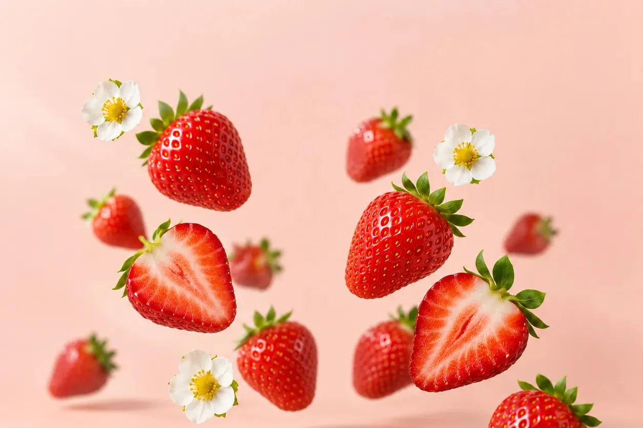 Fresh strawberries and strawberry blossoms against a soft pink wall
